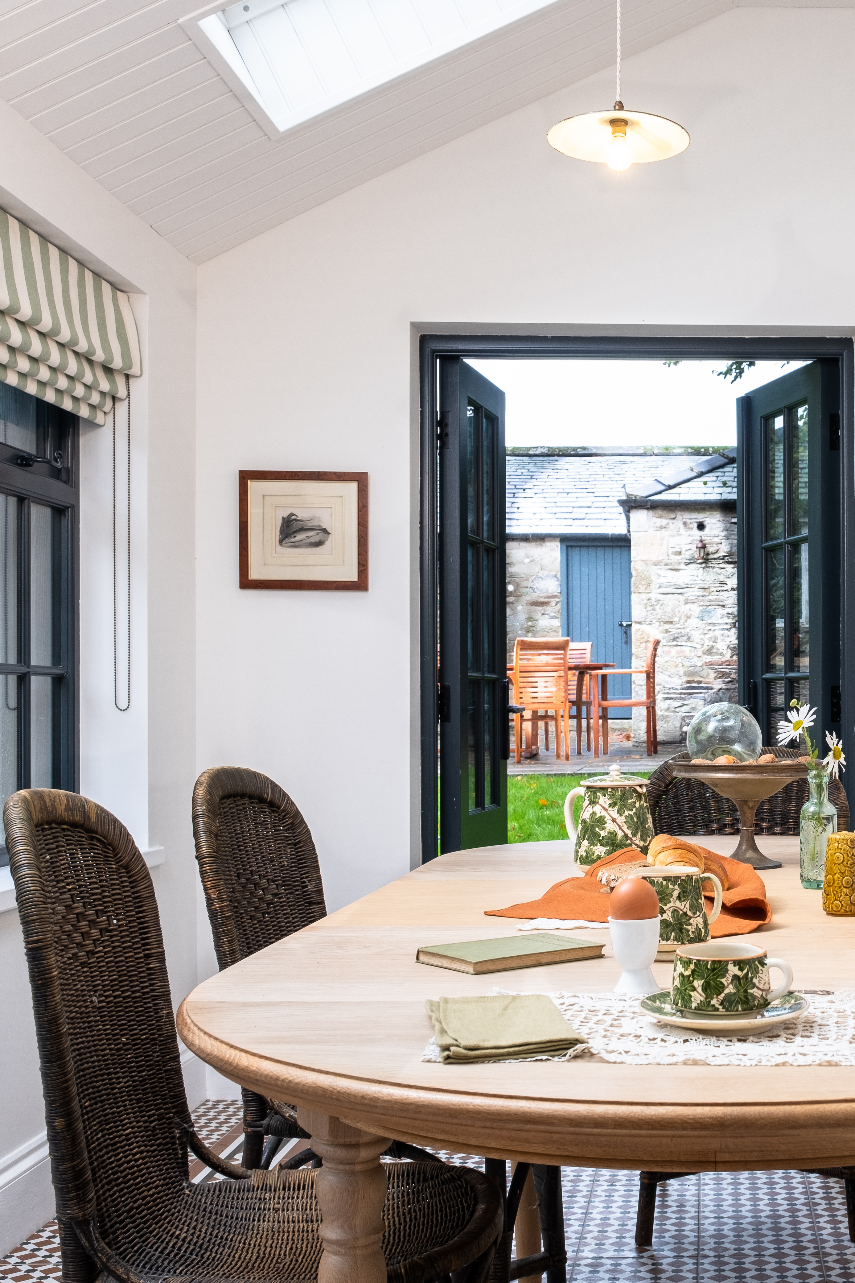 A modern, white dining room with black window frames and a beautiful skylight, with doors opening up into the garden. 