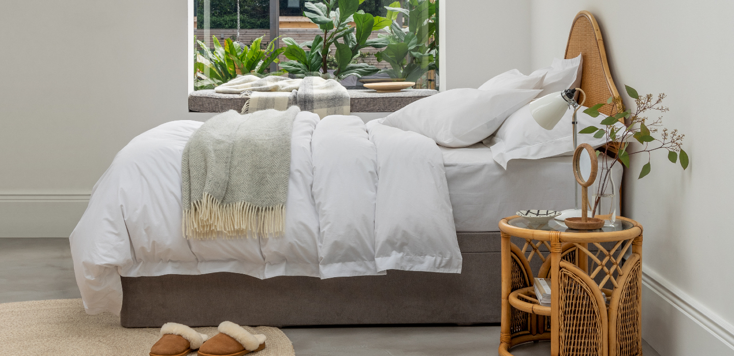 Stylised bedroom with fluffy duvet, throws, plants and sheepskin slippers