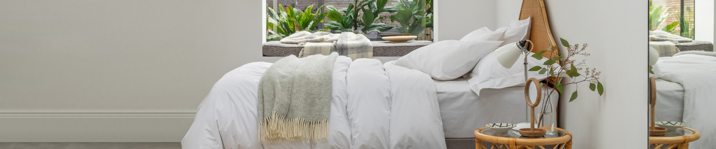 Bed layered with lofty duvet and pillows and styled with a light green bedspread and Soak&Sleep Sheepskin slippers