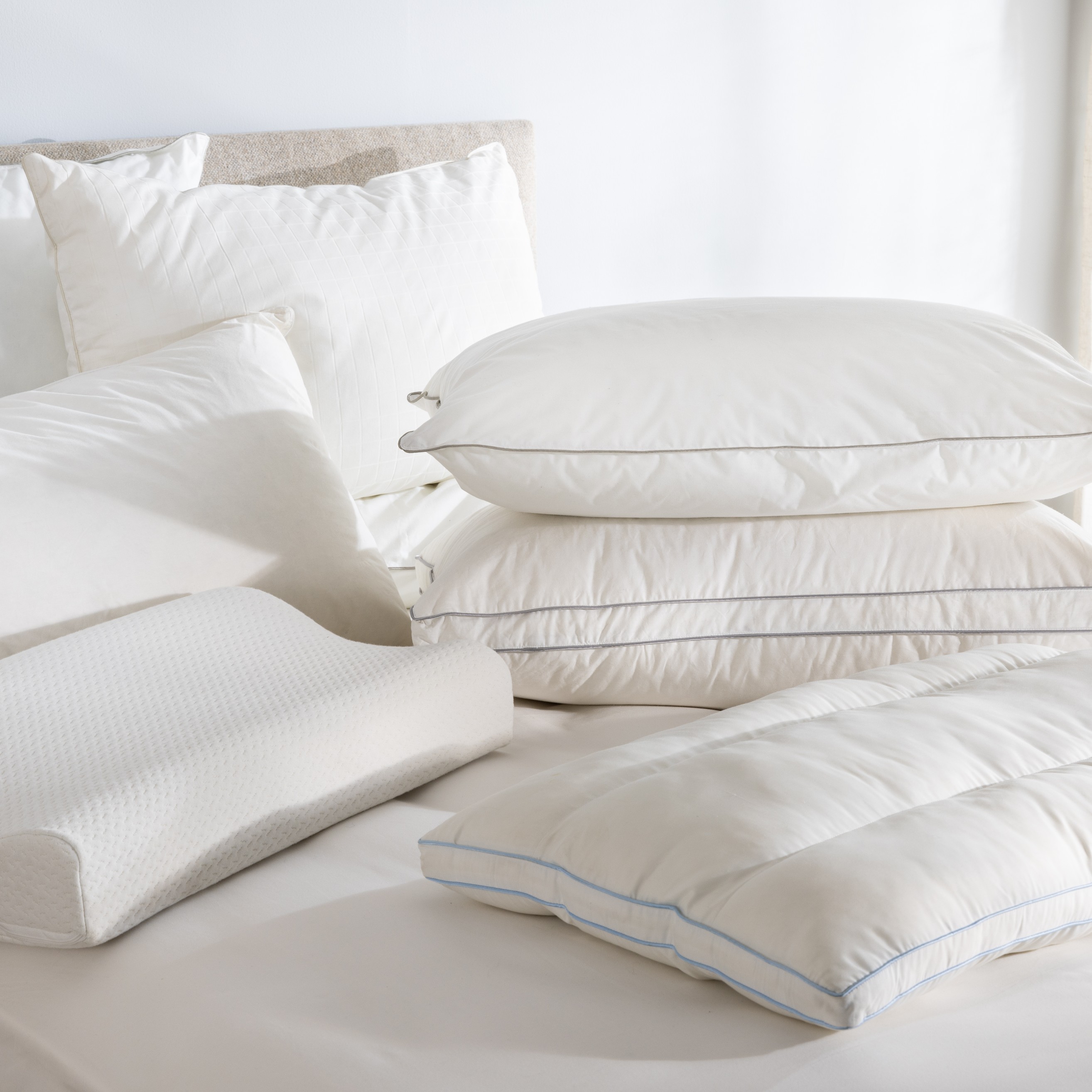Variation of Soak&Sleep pillows, layered and styled on a bed