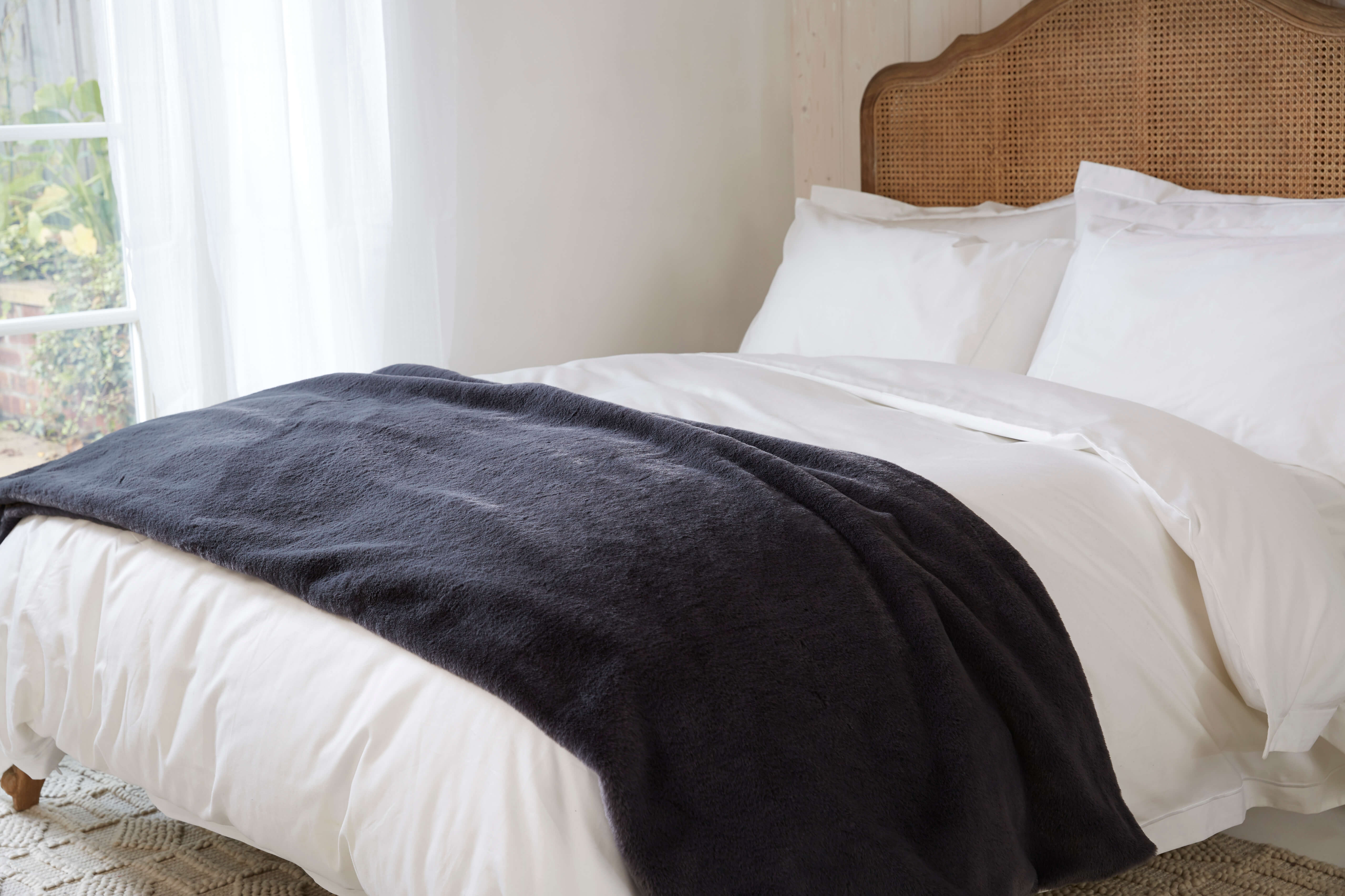 Midnight Grey Fau-Fur Throw, draped over the end of a bed of white Soak&Sleep bedding