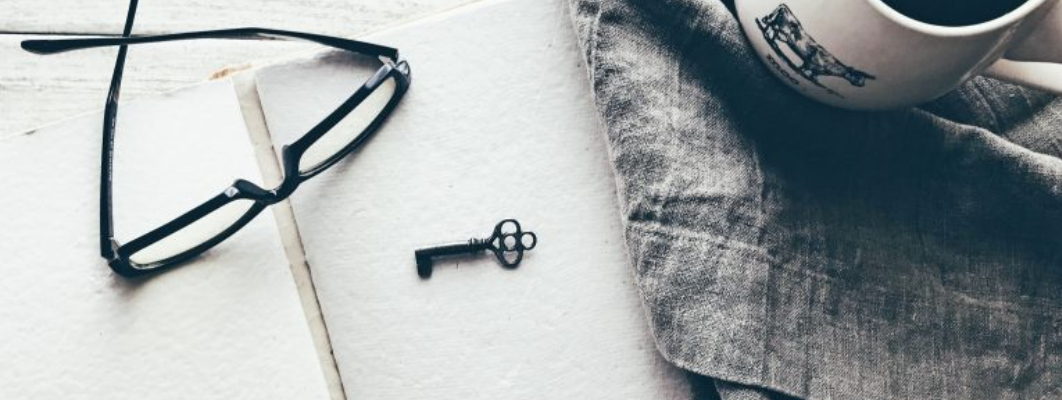 Monochrome image of stylised notebook, key and mug of coffee