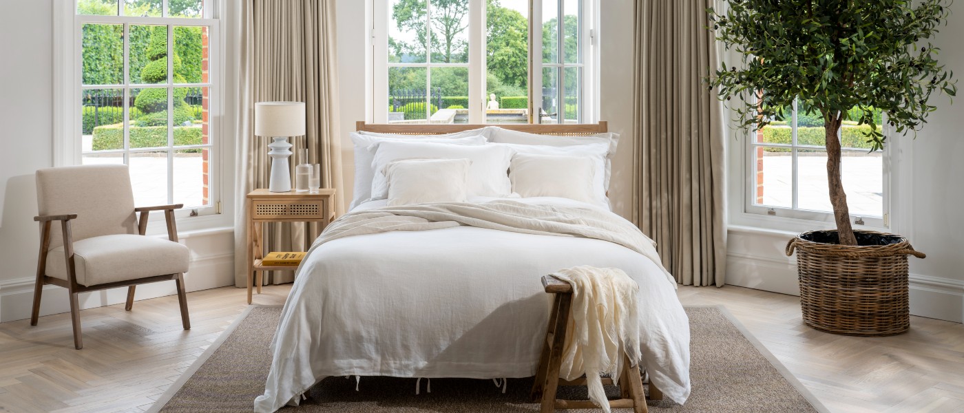 Elegant bedroom with natural coloured features, floor length curtains and an olive tree. Soak&Sleep's white French Linen, styled with natural coloured bedding.
