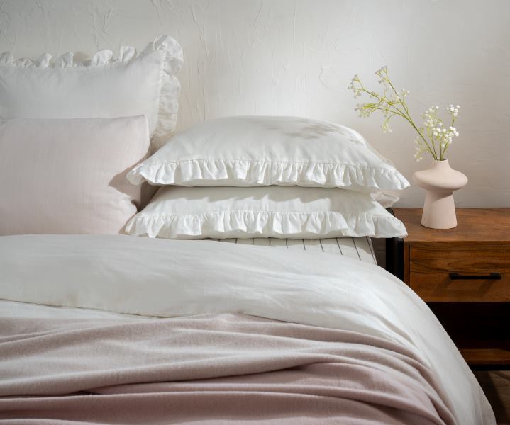 Soak&Sleep's white Ruffled French Linen pillowcases elegantly styled with a pinstripe fitted sheet, a blush pink French linen housewife pillowcase and soft pink pure wool throws.