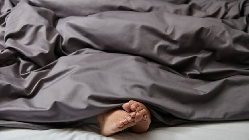 bare feet sticking out from under a dark grey duvet cover