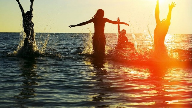 group of people splashing in ocean at sunset