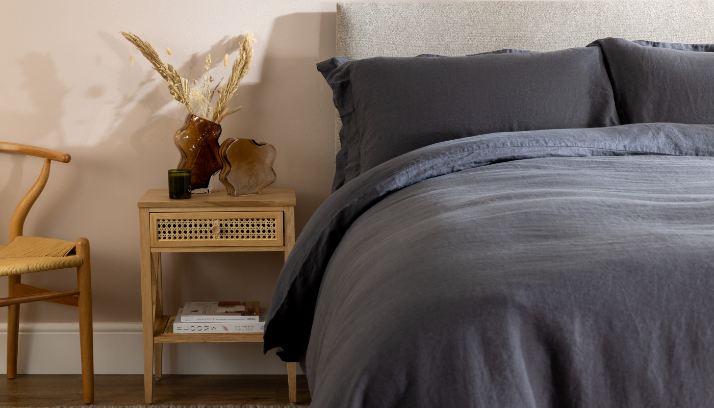 Midnight Grey French Linen bedding by Soak&Sleep. Styled with a rattan side table & chair, brown wavy glass vases and pampas grass.